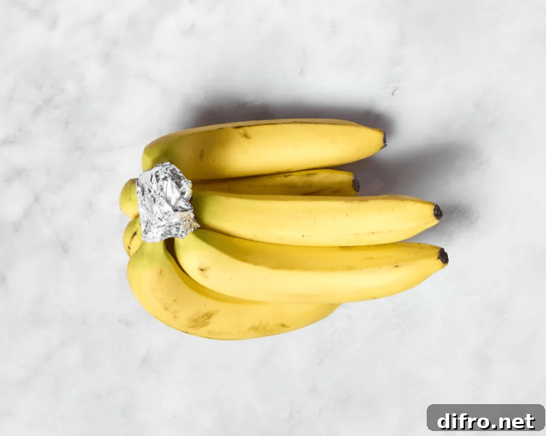 A bunch of bananas on a marble countertop with tin foil wrapped around the joint stems.