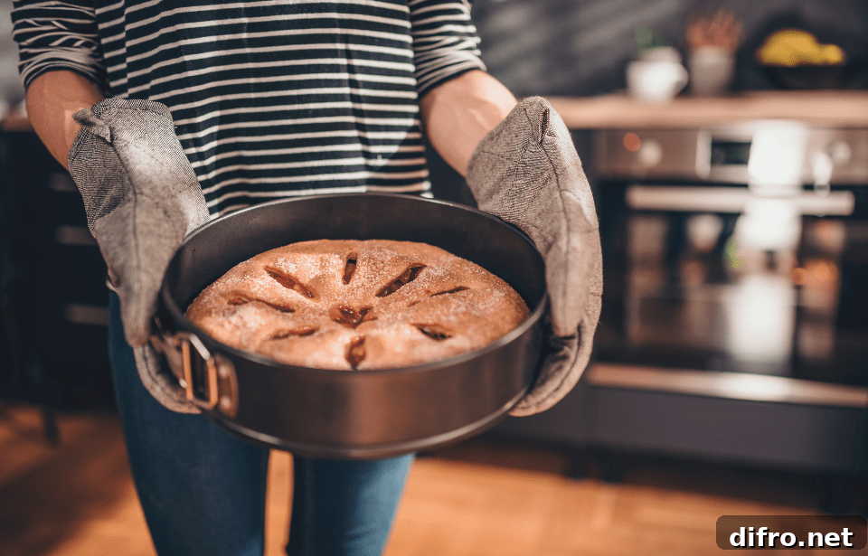 Someone holding a pie in a tin, wearing oven mitts, having just removed it from the oven.