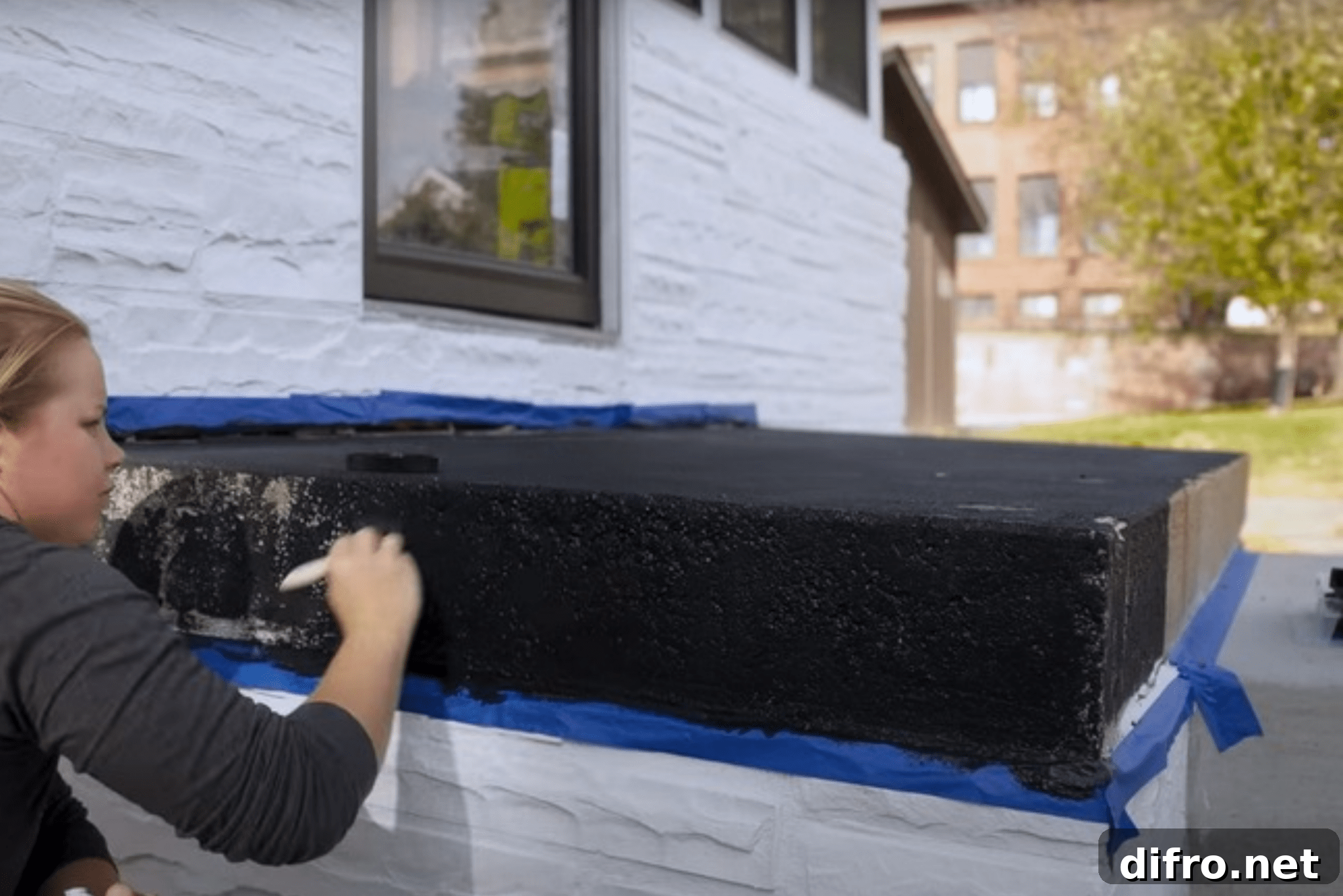 Why Add Sand to Paint: Benefits, Uses, and Tips 5 A woman painting over a box outdoors with textured black paint.